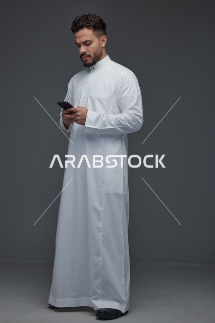رجل سعودي بالثوب الأبيض يستخدم الجوال في الاستوديو