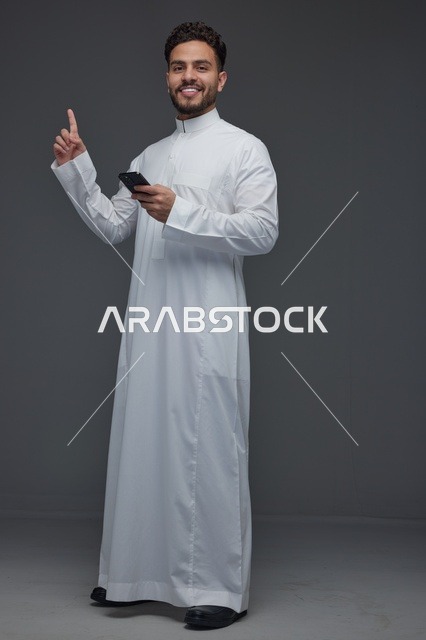رجل سعودي بالثوب يشير للأعلى ومعه هاتف ذكي