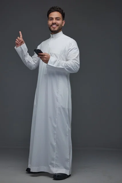 رجل سعودي بالثوب يشير للأعلى ومعه هاتف ذكي