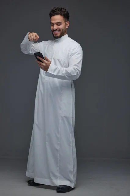 رجل سعودي بالثوب التقليدي يشير إلى هاتف ذكي