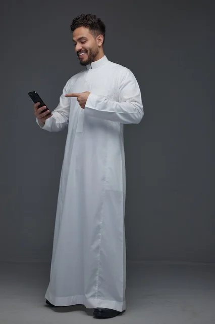 Smiling Saudi Man in Thobe Pointing at Smartphone Studio