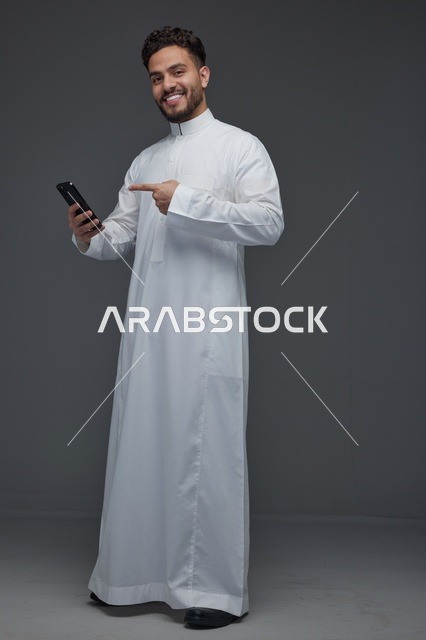 رجل سعودي بالثوب الأبيض يشير إلى هاتف ذكي