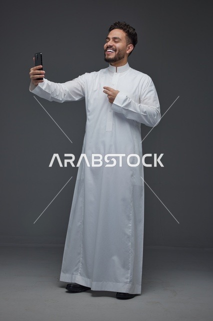 رجل سعودي يرتدي الثوب التقليدي يلتقط سيلفي بالجوال