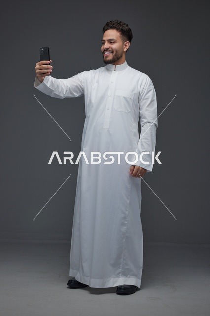 رجل سعودي يرتدي الثوب التقليدي يلتقط سيلفي بالهاتف