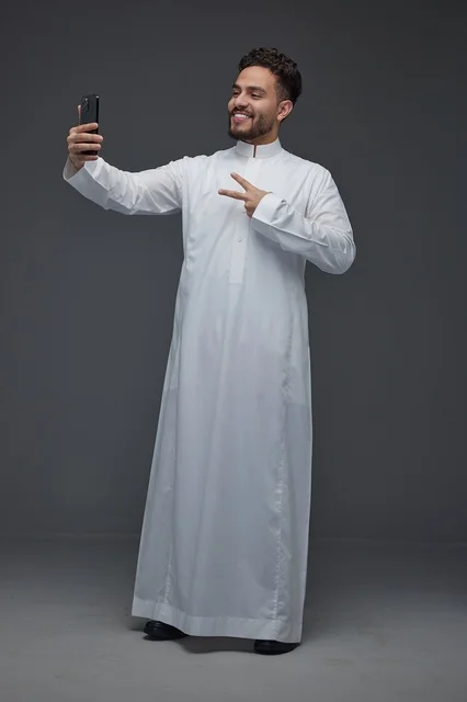 رجل سعودي بالثوب التقليدي يلتقط صورة سيلفي بالاستوديو