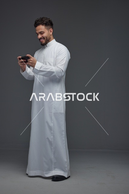 رجل سعودي بالثوب الأبيض يلعب ألعاب الهاتف الذكي