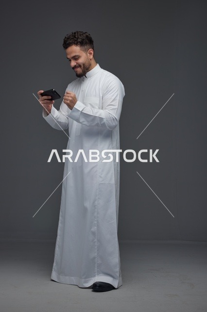 رجل سعودي بالثوب يلعب على الهاتف الذكي في الاستوديو