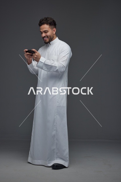 رجل سعودي يلعب بالهاتف الذكي بالثوب التقليدي