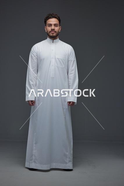 رجل سعودي بالثوب الأبيض التقليدي بخلفية استوديو رمادية