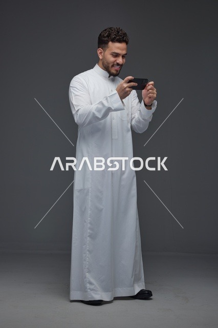 رجل سعودي بالثوب التقليدي يلعب بالجوال في الاستوديو