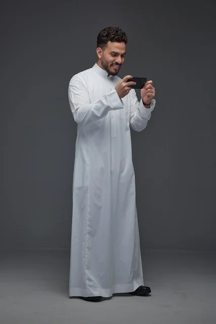رجل سعودي بالثوب التقليدي يلعب بالجوال في الاستوديو
