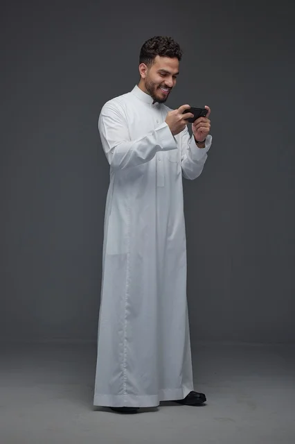 رجل سعودي يرتدي الثوب التقليدي يلعب بهاتفه الذكي