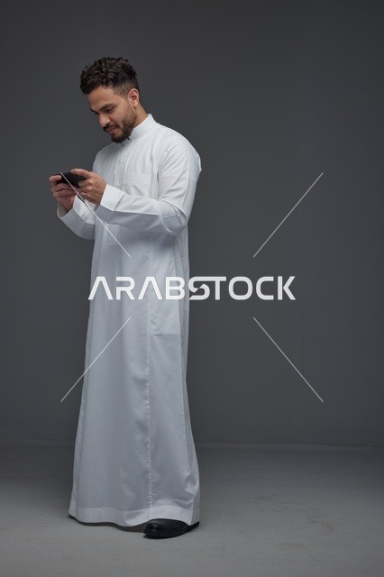 رجل سعودي بالثوب التقليدي يلعب بالهاتف