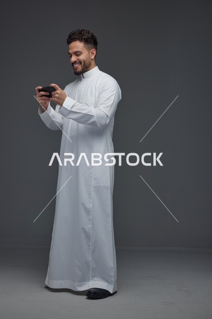 رجل سعودي يرتدي الثوب الأبيض ويلعب بهاتفه الذكي