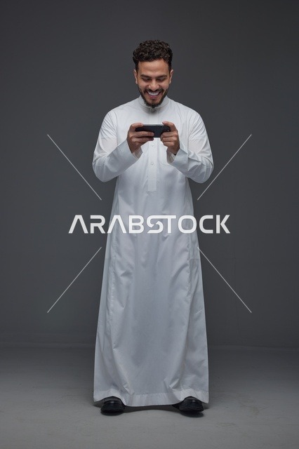 رجل سعودي بالثوب التقليدي يلعب على الهاتف الذكي
