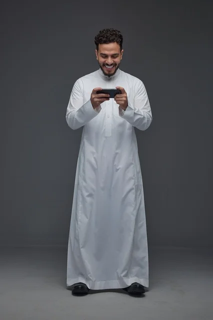 رجل سعودي بالثوب التقليدي يلعب على الهاتف الذكي