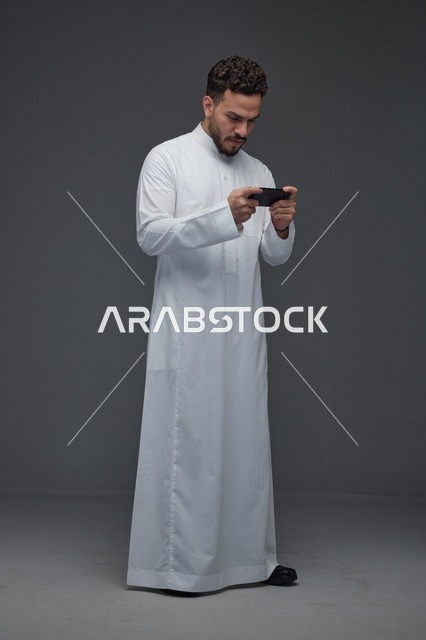 رجل سعودي يرتدي الثوب الأبيض التقليدي يلعب بهاتفه الذكي