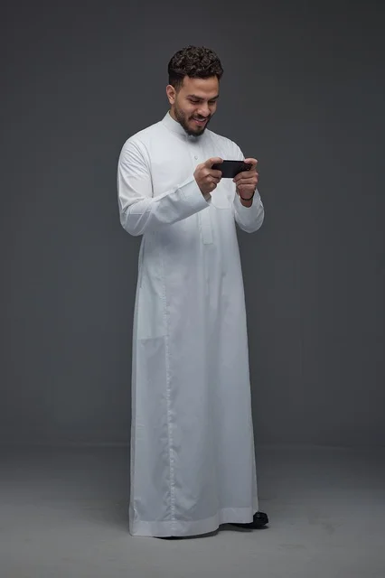 رجل سعودي بالثوب التقليدي يلعب بألعاب الهاتف الذكي