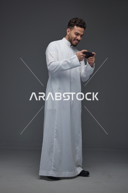 رجل سعودي يلعب بالهاتف الذكي بالثوب التقليدي