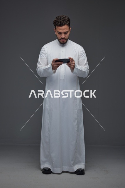 رجل سعودي بالثوب التقليدي يلعب على الهاتف الذكي
