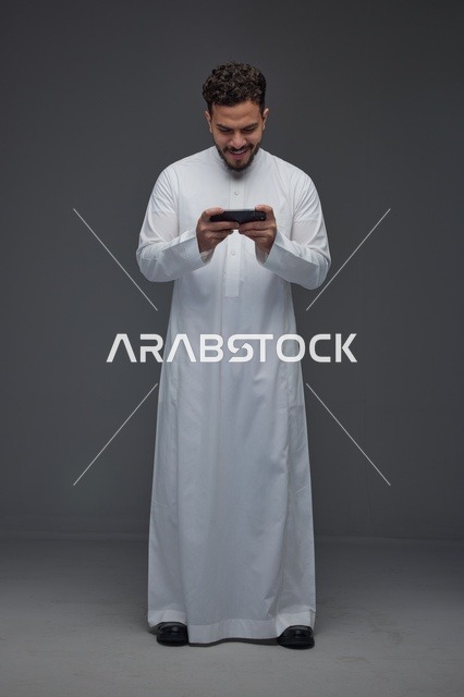 رجل سعودي بالثوب التقليدي يستخدم الهاتف الذكي