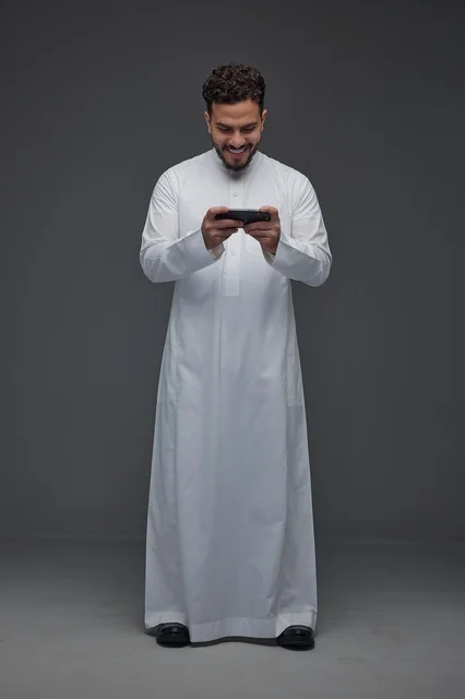 رجل سعودي بالثوب التقليدي يلعب على الهاتف الذكي