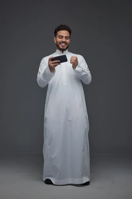رجل سعودي يلعب بالهاتف الذكي بالثوب التقليدي