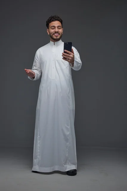 Smiling Saudi Man in Thobe Using Smartphone in Studio