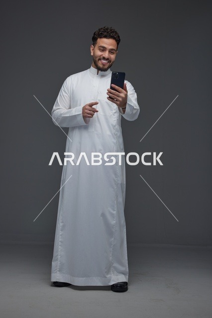 رجل سعودي بالثوب يستخدم الهاتف الذكي في الاستوديو