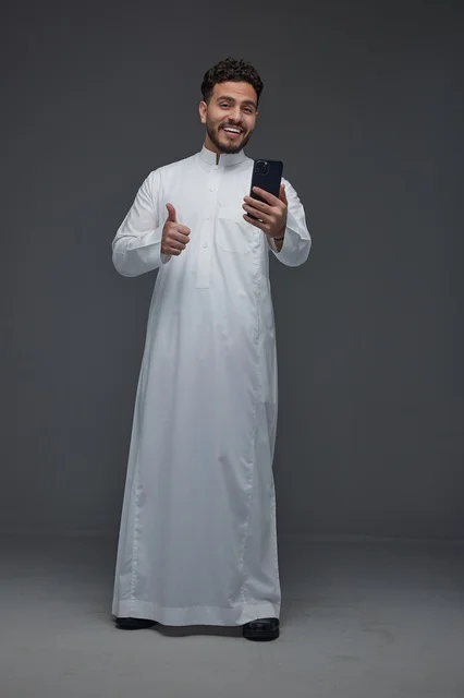 Smiling Saudi Man in Traditional Thobe Using Smartphone