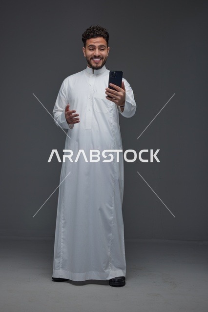 رجل سعودي بالثوب التقليدي يستخدم الهاتف الذكي