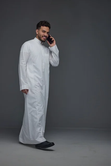 Saudi Man in Thobe Talking on Phone on Gray Background