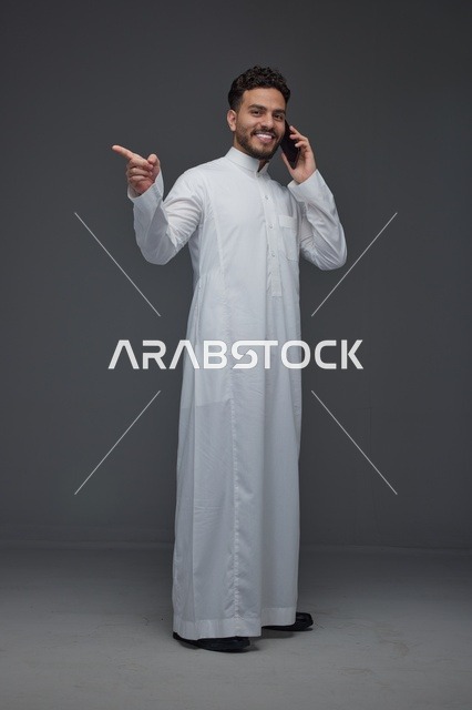 رجل سعودي بالثوب التقليدي يتحدث بالهاتف ويشير للجانب