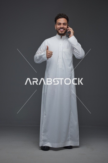رجل سعودي بالثوب يتحدث بالهاتف مع إيماءة النجاح