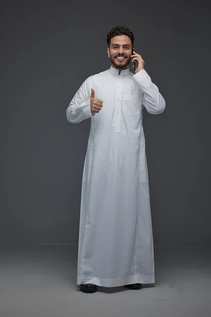 رجل سعودي بالثوب يتحدث بالهاتف مع إيماءة النجاح