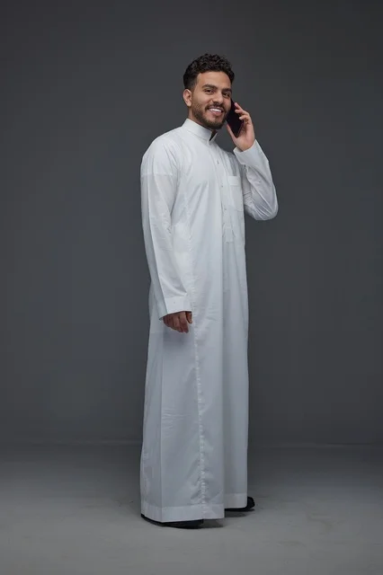 رجل سعودي يبتسم يتحدث بالهاتف الذكي بالثوب التقليدي