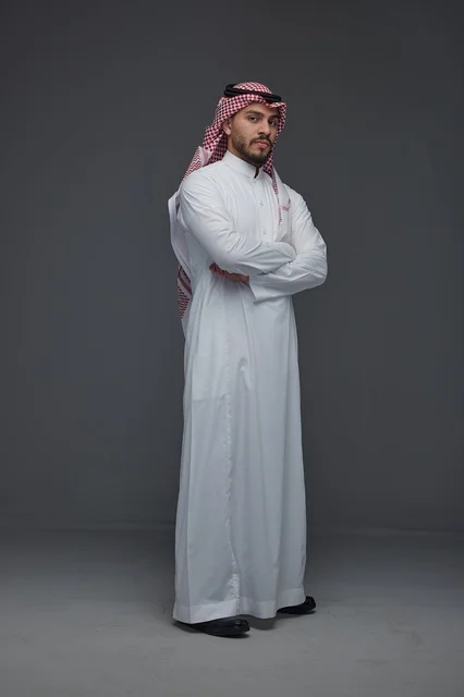 رجل سعودي بالزي التقليدي أمام خلفية رمادية
