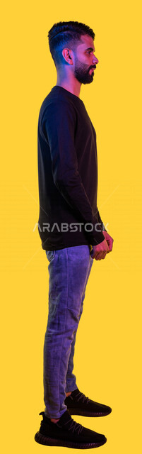 Portrait from the side of a young Saudi Arabian Gulf man standing straight and confident, full length portrait, full body, yellow background