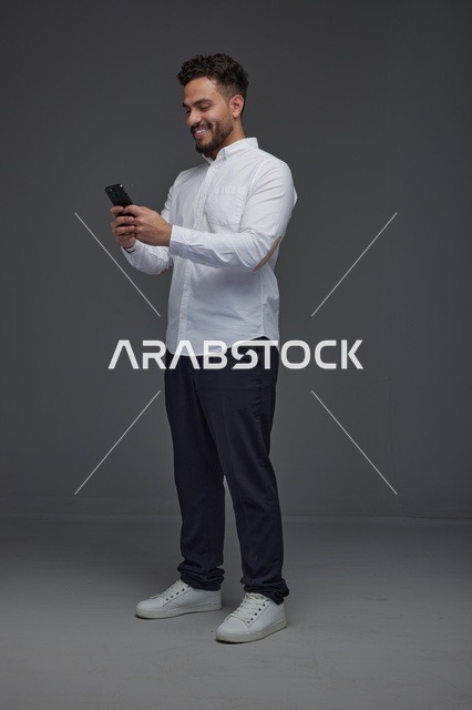 رجل سعودي يستخدم الهاتف الذكي بخلفية استوديو رمادية