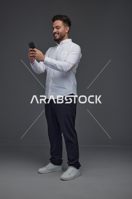 رجل سعودي يستخدم الهاتف الذكي أمام خلفية رمادية