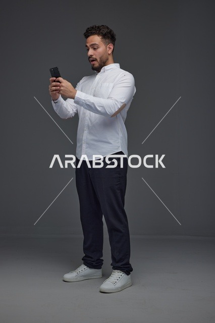 رجل سعودي مندهش ينظر إلى الهاتف الذكي في الاستوديو