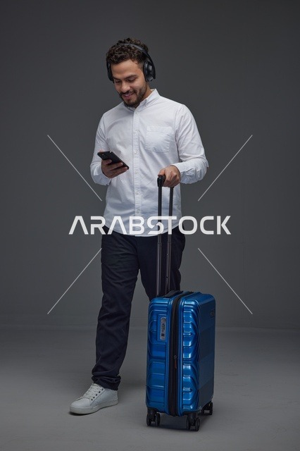 مسافر سعودي يستخدم الهاتف الذكي مع حقيبة سفر