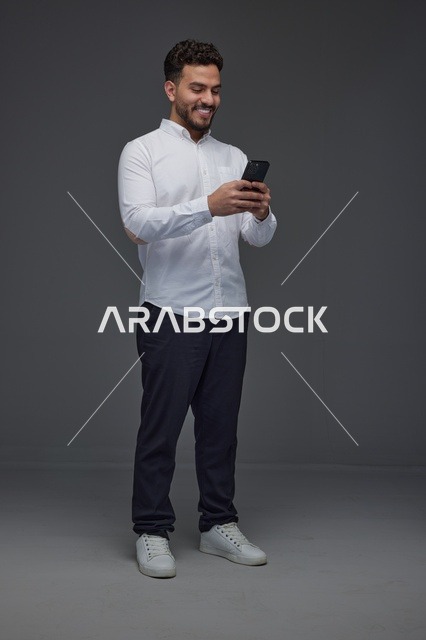 رجل سعودي يستخدم هاتفاً ذكياً بخلفية استوديو رمادية