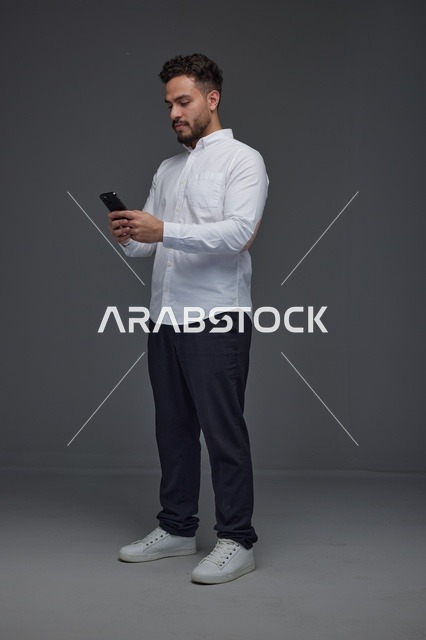 رجل سعودي يستخدم الهاتف الذكي في استوديو بخلفية رمادية