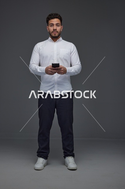 رجل سعودي يستخدم الهاتف الذكي في استوديو رمادي