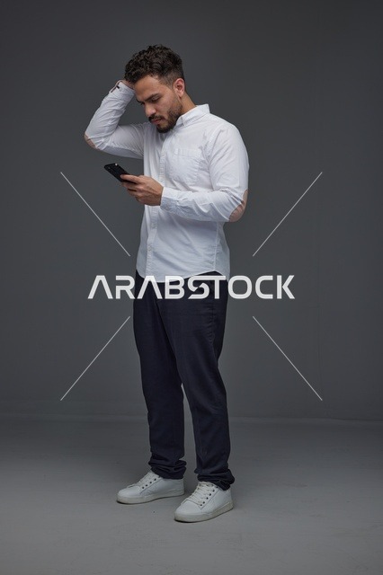 رجل سعودي يستخدم الهاتف الذكي أمام خلفية رمادية داكنة