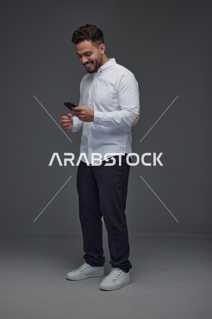 رجل سعودي مبتسم يستخدم الهاتف الذكي بخلفية رمادية