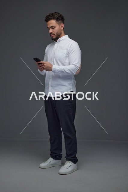 رجل سعودي يستخدم الهاتف الذكي بخلفية استوديو رمادية
