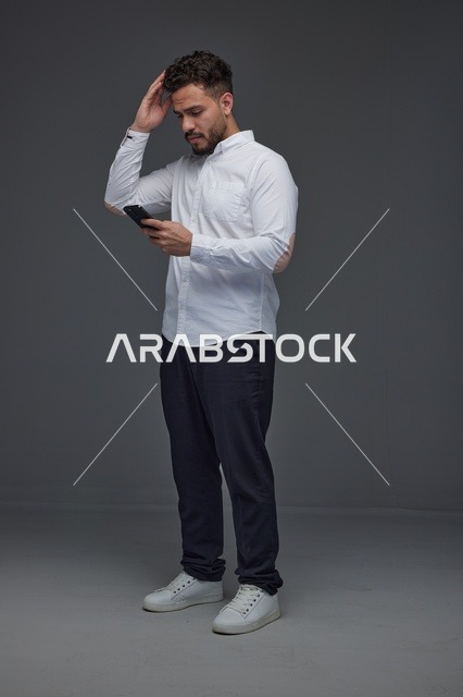 رجل سعودي يستخدم الهاتف الذكي في استوديو رمادي