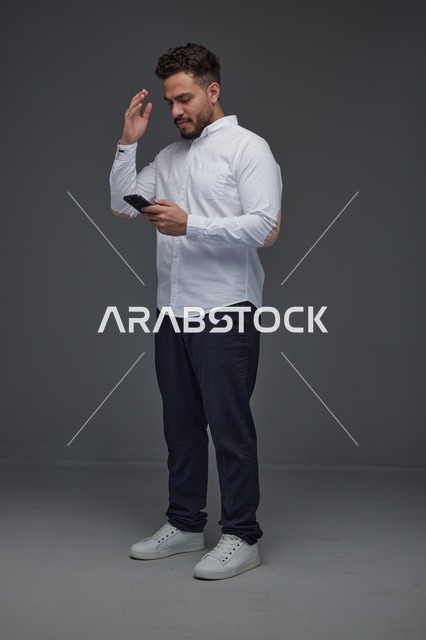 رجل سعودي يستخدم الهاتف الذكي في استوديو بخلفية رمادية